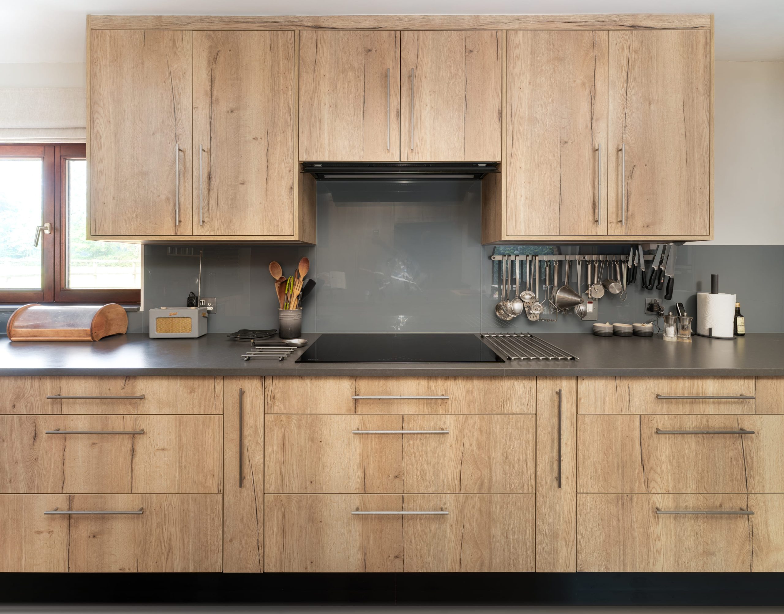 Light oak shaker kitchen cabinets with grey glass splashback and black worktop, installed by Jones Britain kitchen designers in Tunbridge Wells