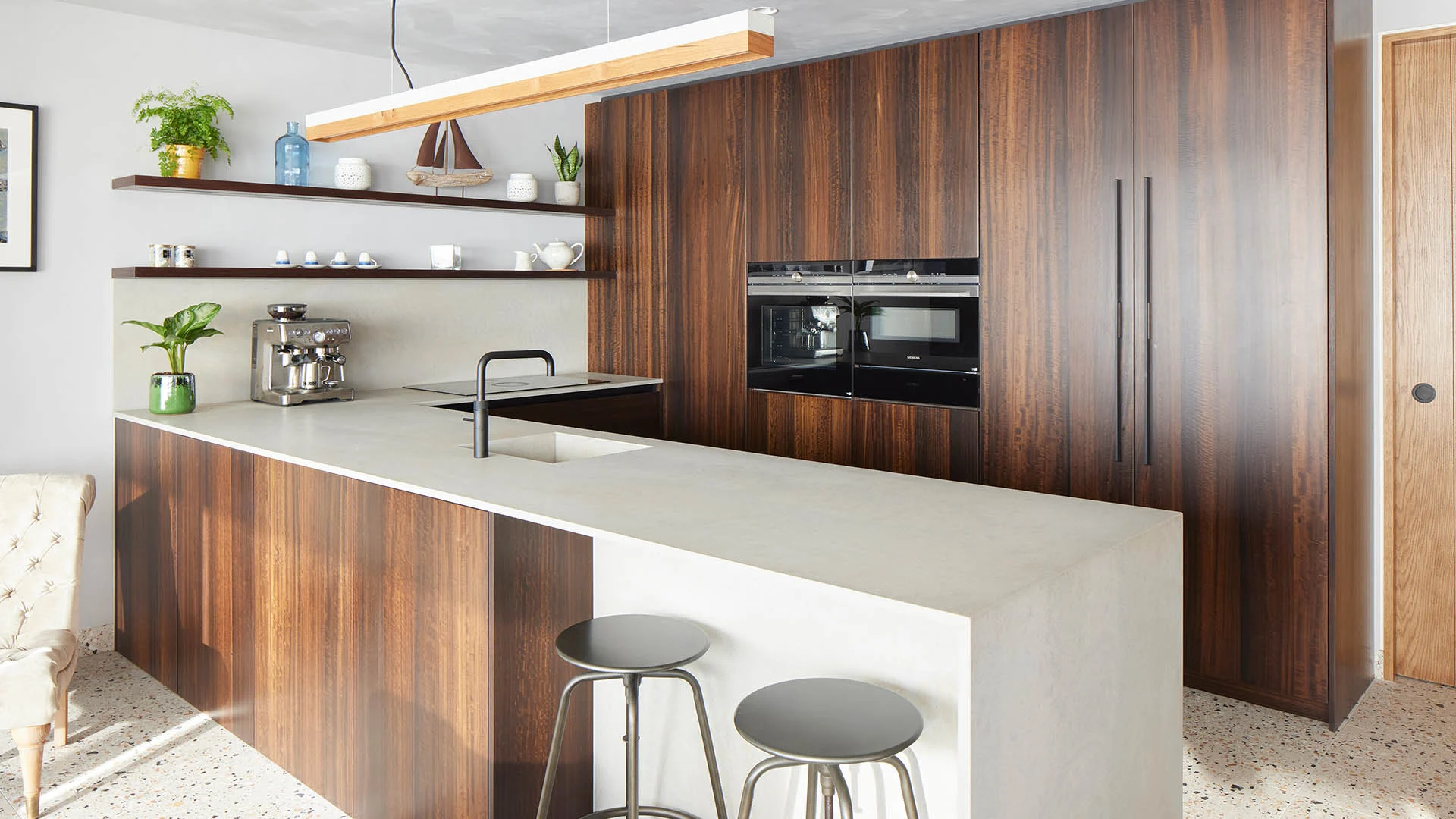 Dark walnut handleless kitchen with pale stone worktop, integrated Siemens appliances, and open shelving, designed by Jones Britain